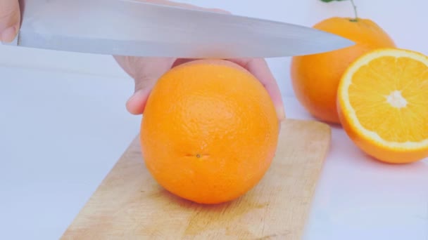 鋭いナイフで木製のまな板の半分に黄金の黄色の熟したオレンジをカットします — ストック動画