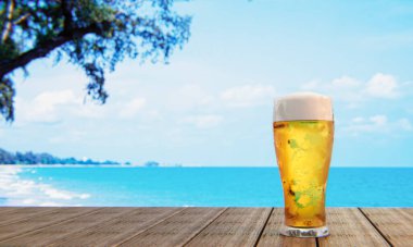 Bira bardağının üzerinde bira köpüğü ve bardakta baloncuklar var. Bardakta soğuk bira, plajdaki ahşap bir masaya yerleştirilmiş, gün boyunca deniz. 3B Hazırlama