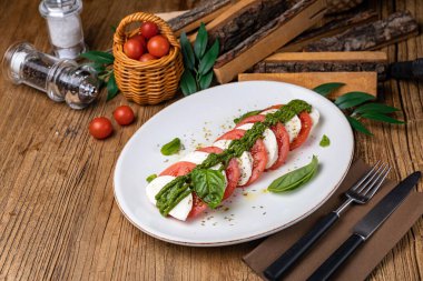 Mozzarella, domates, fesleğen sosu beyaz tabakta.