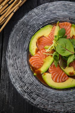 Koyu bir masada doğranmış somon ve avokado tabağı.