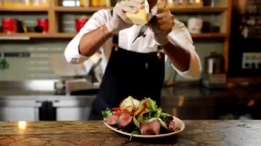 Şef önlüklü ve eldivenli. Mutfakta bir dilim pizza tutuyor.