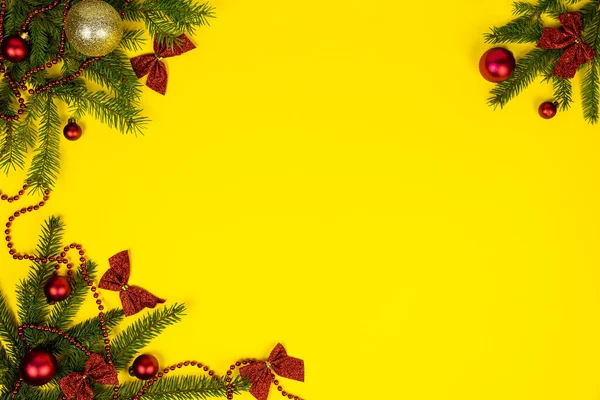 New Years yellow festive background with red matte balls and shiny bows on spruce branches. Flat lay. Copy space. — Fotografia de Stock