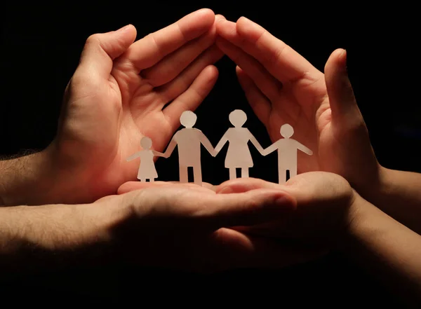 A cut out paper family holding hands, forming a chain, with the hands of a man and a woman forming a house, giving the concept of protection, security, protection and family care.