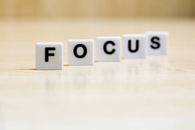      Odaklanma kelimesini oluşturan harfleri içeren bir sıra küçük beyaz plastik karo, görsel odaklanma kavramını veya bir konuyu temsil eder..