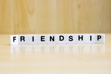  Arkadaşlık kavramını temsil eden arkadaşlık kelimelerini oluşturan harfleri içeren bir dizi küçük beyaz plastik karo..