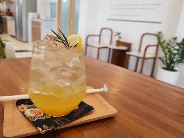 Yuzu orange drink with soda with ice. The drink splits the orange juice and soda into two different colors. The background is a blurry cafe.