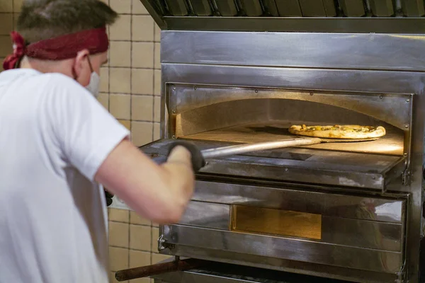 a pizza chef in a mask takes out / puts the pizza in a hot oven.copy space