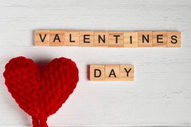 Sevgililer günü sözcüğünün üst görüntüsü kare ahşap fayanslardan ve eski beyaz ahşap arka planda kırmızı büyük örülmüş kalplerden oluşuyordu..