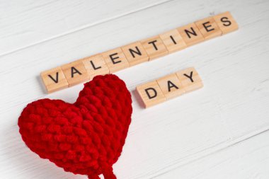 Sevgililer günü sözcüğünün üst görüntüsü kare ahşap fayanslardan ve eski beyaz ahşap arka planda kırmızı büyük örülmüş kalplerden oluşuyordu. Seçici odak