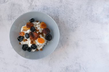 Gri tabakta kurutulmuş meyveli süzme peynir. Sağlıklı ve dengeli yiyecekler. Süzme peynir bir protein kaynağıdır. Kuru üzüm, kurutulmuş kayısı ve kuru erik kışın vitaminlerdir. Sağlıklı yaşam tarzı kavramı