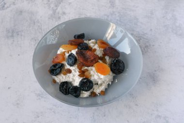 Gri tabakta kurutulmuş meyveli süzme peynir. Sağlıklı ve dengeli yiyecekler. Süzme peynir bir protein kaynağıdır. Kuru üzüm, kurutulmuş kayısı ve kuru erik kışın vitaminlerdir. Sağlıklı yaşam tarzı kavramı