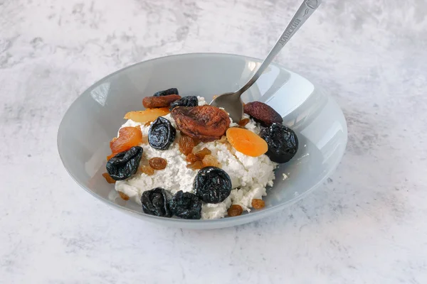 Gri tabakta kurutulmuş meyveli süzme peynir. Sağlıklı ve dengeli yiyecekler. Süzme peynir bir protein kaynağıdır. Kuru üzüm, kurutulmuş kayısı ve kuru erik kışın vitaminlerdir. Sağlıklı yaşam tarzı kavramı