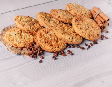Kahve çekirdekleri, anason, tarçın çubukları ile süslenmiş taze pişmiş yulaf ezmesi kurabiyeleri, fotokopi alanı ile beyaz ahşap masa zemininde karanfiller. Menü düzeni için resim tasarımı. Lezzetli ve abur cubur kavramı.