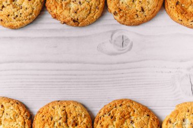 Beyaz ahşap masa zemininde çikolata parçacıklı ve yulaf ezmeli kurabiyelerden oluşan bir çerçeve. Ticari veya menü tasarımı için resim kullanımı. Kış, sonbahar, mutfak. Düz yatıyordu.