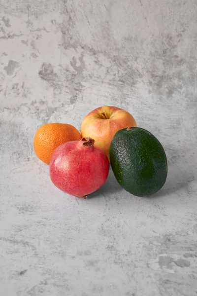 Ön manzara. Elma, mandalina, avokado, nar yan yana dizilmiş gri çizilmiş arka planda fotokopi alanı. Sonbahar-kış döneminde vitamin kavramı, vejetaryenlik, sağlıklı yaşam tarzı.