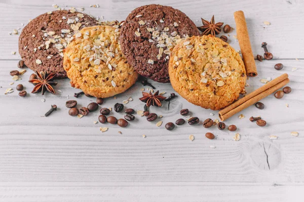 Kahve çekirdekleri, anason, tarçın çubukları, karanfiller, fotokopi alanı olan yulaflı beyaz ahşap bir masada taze pişmiş yulaf ve çikolatalı kurabiyeler. Menü düzeni için resim tasarımı. Üst görünüm, kapat