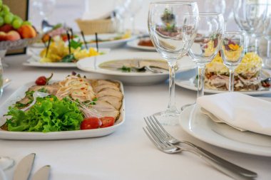 Masanın üzerinde açık renkli tabaklar ve beyaz masa örtüsü ile bir parti, düğün ya da diğer özel bir etkinlik için çeşitli yemekler var. Restoran işletme ve hizmet sektörü kavramı.