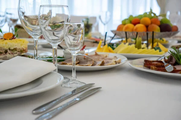 Masanın üzerinde açık renkli tabaklar ve beyaz masa örtüsü ile bir parti, düğün ya da diğer özel bir etkinlik için çeşitli yemekler var. Restoran işletme ve hizmet sektörü kavramı.