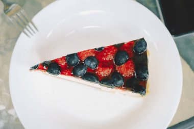 Beyaz tabakta yaban mersini ve ahududu olan bir parça çilekli cheesecake. Kafelerin, pastanelerin menüsü için fotoğraf. Tatlı yemek, hamur işi, tarifler..