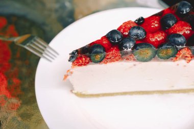Beyaz tabakta yaban mersini ve ahududu olan bir parça çilekli cheesecake. Kafelerin, pastanelerin menüsü için fotoğraf. Tatlı yemek, hamur işi, tarifler..