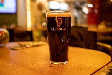 Dubllin, İrlanda - Ocak. 9, 2020: Bardaki ahşap bir masada köpüklü bira bardağı. popüler İrlanda birası