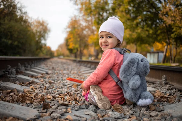 Concepto de juegos infantiles peligrosos. alegre chica se sienta en las vías del tren solo — Foto de Stock