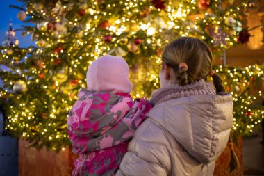 Anne ve bebek kollarında sokak fuarındaki parıldayan Noel ağacına bakıyorlar. arka plan..