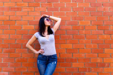 Gözlüklü genç, ince bir kadın tuğla duvara bakıyor.