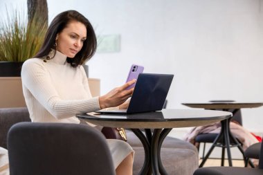 Masada dizüstü bilgisayarla otururken telefonda yazan güzel bir iş kadını..