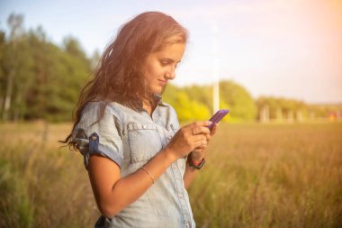 Mutlu genç kadın güneşli bir günde doğadaki akıllı telefona bakar..
