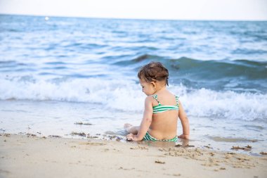 Küçük kız sahilde oturmuş dalgaları seyrediyor. arka plan.