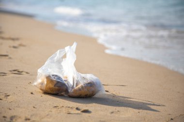 Plastik torba kumlu bir plajda yatıyor. Çevre kirliliği. Denizde çöp.