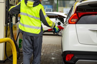 Tulumlu bir benzin istasyonu çalışanı arabaya benzin dolduruyor. Yüzü yok