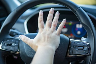 Kadın eli modern bir arabanın direksiyonunda kornaya basar. Yüzü yok
