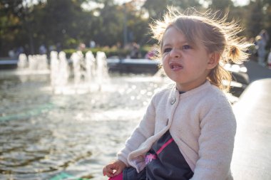 Eğlence düşkünü kız. Parkta fıskiyelerle sinirli görünüyor.