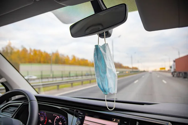 medical mask hangs on the salon rearview mirror in the car on the highway. close up