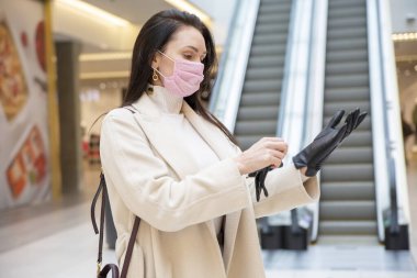 Tıbbi maskeli kadın alışveriş merkezinde ya da havaalanında siyah deri eldivenler giyiyor.