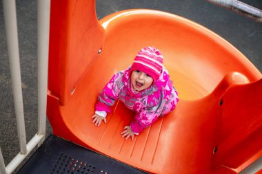 Soğuk havalarda kaydırağın üstünde oynayan mutlu çocuk.
