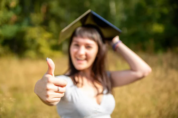 Concetto di educazione online. pollice in su sullo sfondo in sfocatura giovane studentessa felice donna tiene un computer portatile sopra la testa come un cappello accademico quadrato — Foto Stock