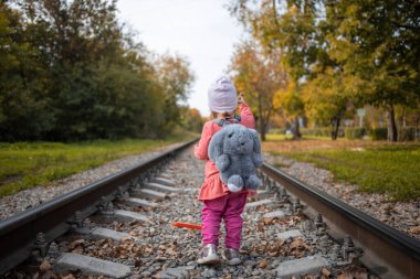Küçük kız demiryolunda yalnız yürüyor.