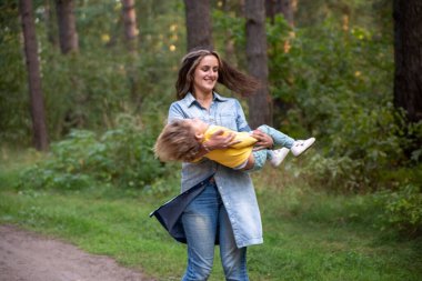 Genç anne kucağında bir bebekle dönüyor. Doğa ve ormanın arka planında küçük bebekle dans eden mutlu bir anne. Anne ve kızı gülüyor. Tasasız ebeveynlik