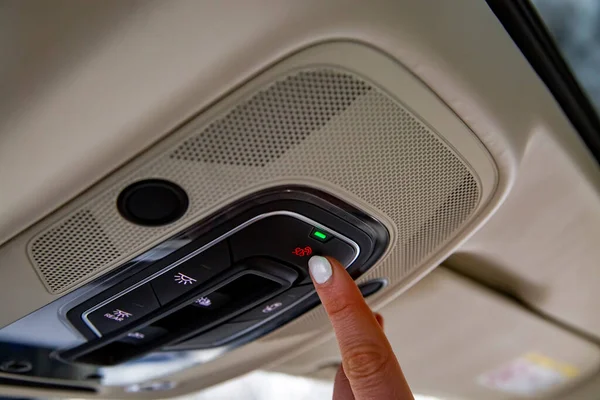 female driver\'s finger presses sos button on the ceiling panel of a modern car