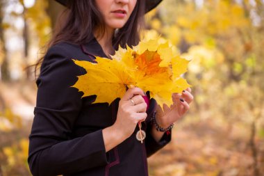 Güzel sonbahar afişi. Siyahlı genç kadın elinde altın akçaağaç yaprakları tutuyor. Yüz portresi. Bulanık orman