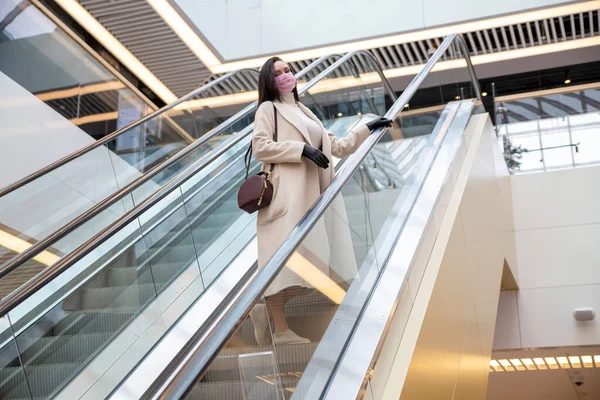 portrait of middle aged woman with gloves and mask on escalator in public place