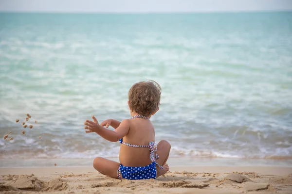 海のビーチで砂の中で遊んでいる青い水着のかわいい幼児の女の子 バックビュー — ストック写真