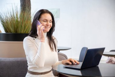 Ofisteki laptopta gülümseyen ve konuşan orta yaşlı güzel bir kadının portresi.