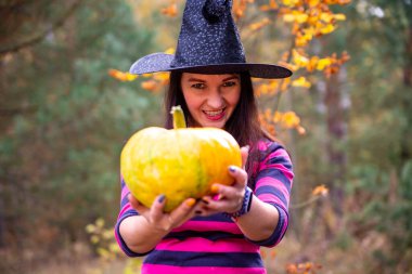 Güzel cadı, sonbahar ormanında kameraya bir balkabağı uzatır.