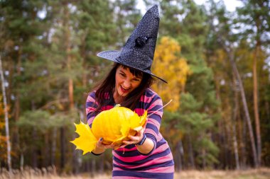 Cadı kadın sonbahar ormanında balkabağını korkunç duygularla tutuyor.
