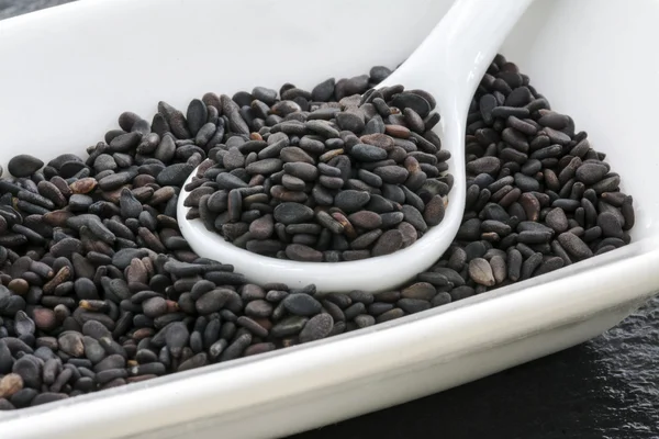 Semillas de sésamo negro en una cuchara blanca — Foto de Stock