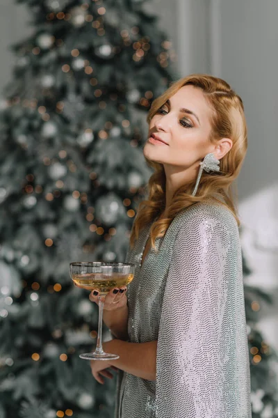 クリスマスツリーのぼんやりとした光のボケを背景に ガラスを手にした豪華な衣装で美しいブロンドの女性を笑顔にします 2021年の新年 ソフトフォーカス アートノイズ — ストック写真